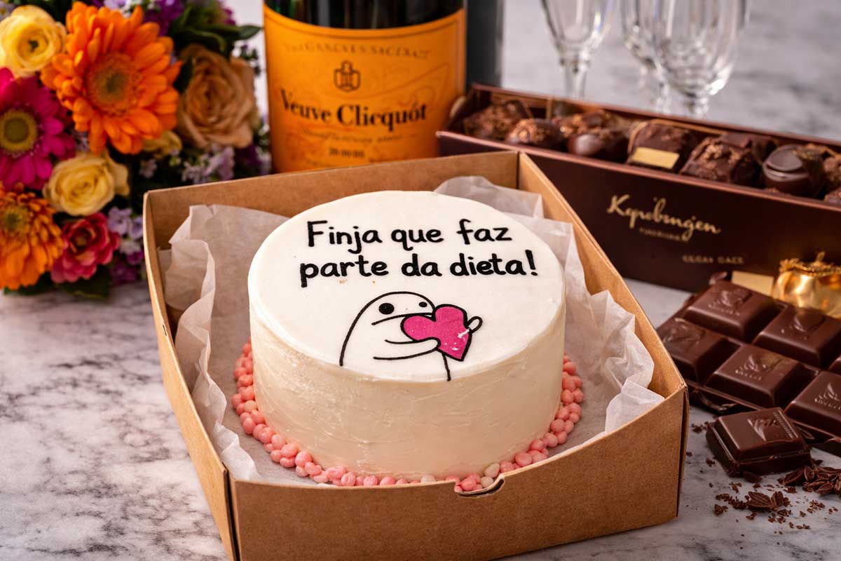 Mini Bolo Bentô Cake branco em hamburgueira, com desenho Flork e a frase preta 'Finja que faz parte da dieta!'. Ao redor, um suntuoso buquê de flores coloridas, uma garrafa de Champagne Veuve Clicquot com seu rótulo amarelo icônico, uma caixa de bombons Kopenhagen aberta exibindo detalhes de chocolate nobre e taças de cristal ao fundo. 📑